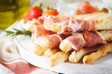 Traditional Italian snacks for wine, breadsticks (grissini), tomatoes, prosciutto (jamon), strawberries and olives. Selective focus.