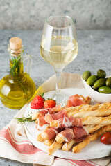 Traditional Italian snacks for wine, breadsticks (grissini), tomatoes, prosciutto (jamon), strawberries and olives.