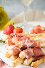 Traditional Italian snacks for wine, breadsticks (grissini), tomatoes, prosciutto (jamon), strawberries and olives. Selective focus.