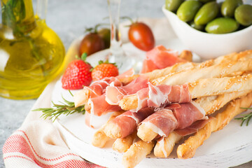 Traditional Italian snacks for wine, breadsticks (grissini), tomatoes, prosciutto (jamon), strawberries and olives. Selective focus.
