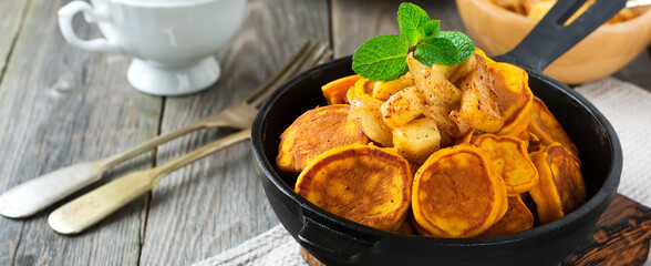 Small pumpkin pancakes with chocolate sauce in a pan on the old vintage wooden background. Selective focus