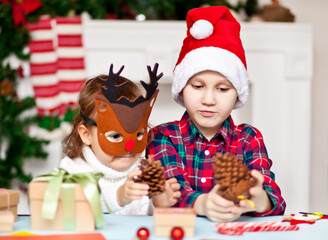 Funny girl and boy in a Christmas deer mask and Santa cap holding pine cones