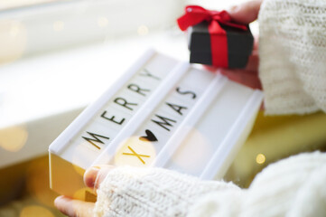 Woman holding lightbox with message merry Xmas. Preparing gifts for winter holidays. Home cozy