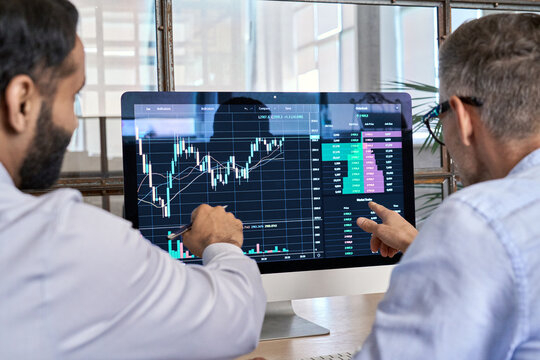 Two traders brokers stock exchange market investors discussing crypto trading charts growth using pc computer pointing at screen analyzing financial risks, investment profit forecast. Over shoulder