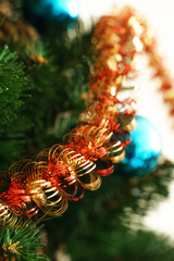 Golden-red tinsel against the background of green branches and needles of an artificial Christmas tree