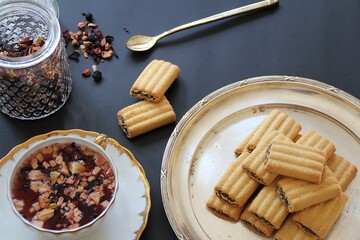 porcelain cup with fruit tea, loose fruit tea, white cup with golden decorations, chocolate-stuffed shortbreads, glass container with fruit tea