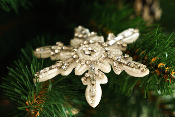 Felt snowflake, embroidered with beads, against the background of branches and needles of an artificial tree