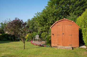 Devon, England, UK. 2021.  A Dutch barn style garden shed with double doors standing with patio, tables and chairs in an English country garden. - obrazy, fototapety, plakaty