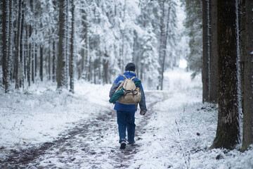 Fototapeta na wymiar A tourist with a backpack walks through the winter forest.