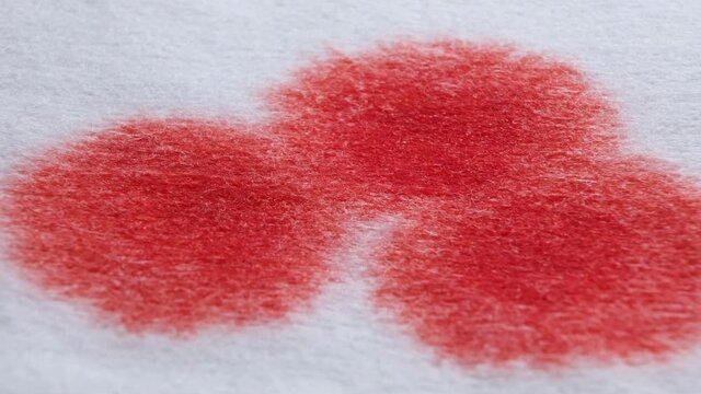 Red blood drops on a white bandage, paper or cloth-like surface. Splattering red color of blood, bloodstains reveal on white background. Shallow depth of field. Macro view.