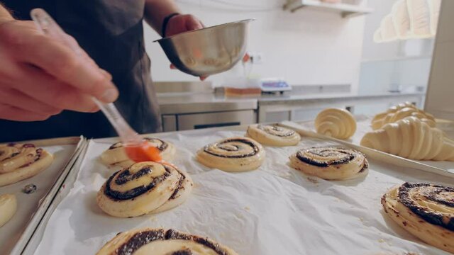 Baker smears egg yolk on raw escargot buns with poppy seed before baking. Baking process. High quality 4k footage
