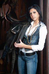 woman in the stable with the saddle before riding a horse. 