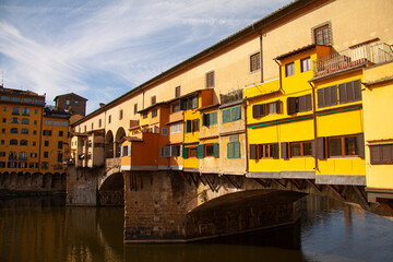 Fototapeta na wymiar View of the Ponte Vecchio - Old Bridge - in Florence (Firenze) - by the river Arno with blue sky and reflections in the water. Famous landmark in Tuscany, Italia.