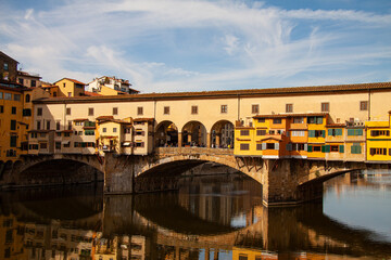 View of the Ponte Vecchio - Old Bridge - in Florence (Firenze), Italy - by the river Arno with reflections in the water and blue sky. Famous landmark in Tuscany.