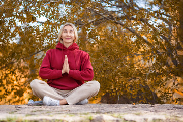 Mental balance. Adult attractive woman sits on the ground and meditating in autumn park outdoor, selective focus.