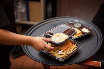 A view of an employee attending to a tray full of to-go containers, in a restaurant kitchen setting.