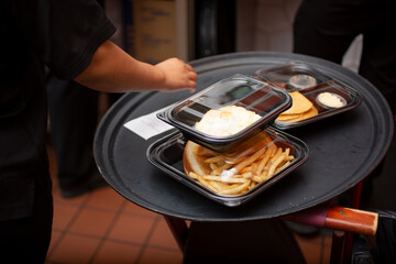 A view of an employee attending to a tray full of to-go containers, in a restaurant kitchen setting.