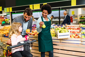 Father and daughter buying fresh fruits. African American grocery store employee is helping them.