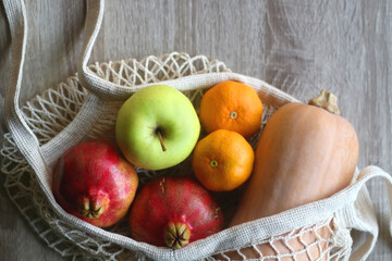 Crochet bag filled with butternut squash, pomegranates, apples and tangeriens. Top view.