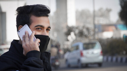 Young man holding mobile phone, using smartphone, making a call, talking on the phone, standing on street with transport traffic on the background