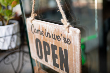 A closeup view of a rustic wooden hanging sign that says Come In We're Open, seen in the lobby of a local retail store. - Powered by Adobe