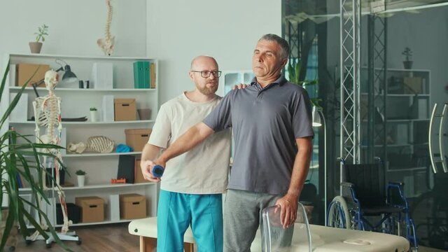 Senior Man a Brain Stroke Doing Dumbbell Exercises as Part of a Rehabilitation Program with a Physiotherapist in a Modern Clinic. Paralysis of the Facial Nerve, Limited Movement. Rehabilitation.