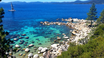 A wide shot of Lake Tahoe in the summer with a sailboat in the background on a sunny day and in the...