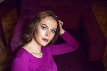 young tall woman is sitting on a chair in hotel near the window in tight purple yoga clothes with a lamp shining from behind