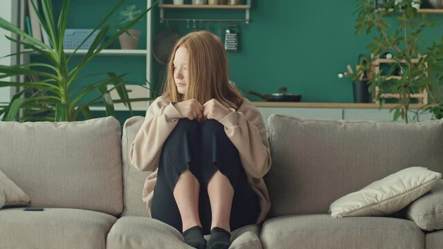 Depressed and Desperate Teenage Girl Wrapping Her Head in Her Arms on the Living Room Couch at Home. Physical and Emotional Abuse, Aggression, Cyberbullying From Social Networks. Mental Health.