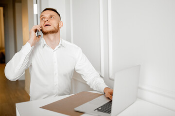 A young man working in the kitchen talking on the phone thought