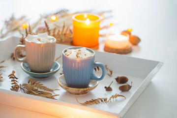 two cups of  coffee  with marshmallows  and autumn decor on white wooden tray