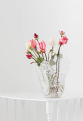 pink and white roses on glass vase on white wooden shelf