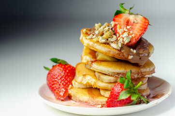 Pancakes stacked with bananas, strawberries and nuts, topped with chocolate and strawberry sauce