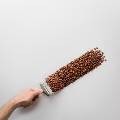 Creative coffee composition on a gray background. A man's hand with a brush paints with coffee beans. Top view.