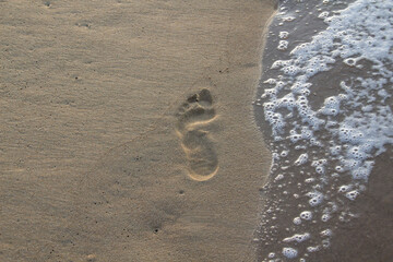 Fototapeta na wymiar Sea foam from a wave on the sand with traces. Human footprint on the sand with sea water.