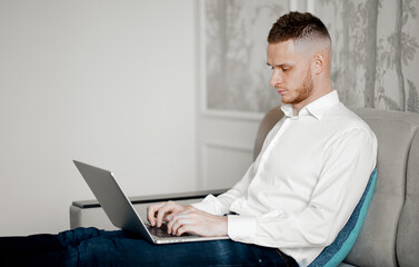 a young man works at a laptop on the couch at home