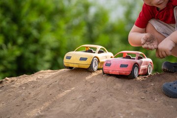 Fototapeta na wymiar Child crouches on a pile of dirt with two toy cars and smiles