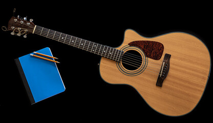 Classical acoustic guitar and a blue notepad on a black background.