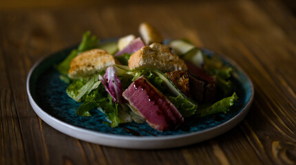 Salad with tuna and croutons. Salad on a blue plate. Restaurant food. Takeout food.