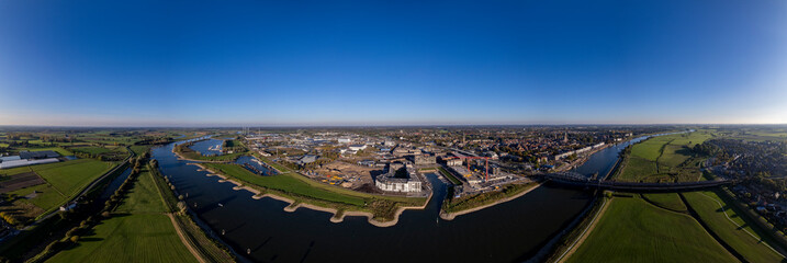 PUUR21 construction site with wide view of Noorderhaven neighbourhood along the river IJssel against a clear blue sky. Aerial of urban development in tower town Zutphen.