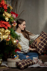 Young Caucasian woman observing a pillow she is holding in her hands next to a Christmas tree