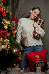 Young caucasian woman smiling next to a christmas tree hugging a christmas pillow