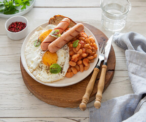 Traditional English breakfast with fried eggs, sausages, beans, fresh herb, red pepper and toast on a wooden  background. Rustic style. Top view
