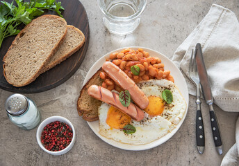 Traditional English breakfast with fried eggs, sausages, beans, fresh herb, red pepper and toast on a gray background. Concept morning and nutrition food. Top view