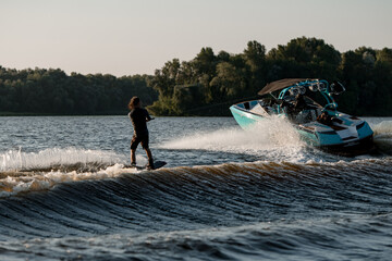 Bright motor boat pulls an active man riding a wakeboard down the river