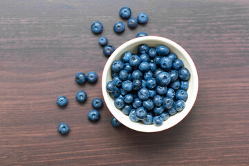 Blueberries in a red bowl on wooden table.