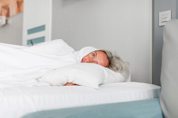 Frightened depressed sad middle aged woman lying alone on bed