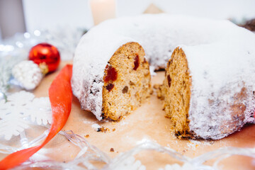 Traditional round Christmas stollen made of dried fruits and nuts sprinkled with powdered sugar on the background of a Christmas decor with candles. Traditional Christmas cupcake.