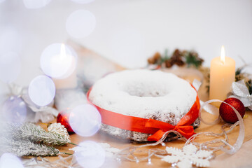 Traditional round Christmas stollen made of dried fruits and nuts sprinkled with powdered sugar on the background of a Christmas decor with candles. Traditional Christmas cupcake.