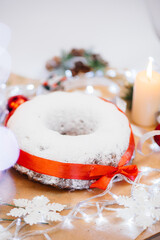 Traditional round Christmas stollen made of dried fruits and nuts sprinkled with powdered sugar on the background of a Christmas decor with candles. Traditional Christmas cupcake.